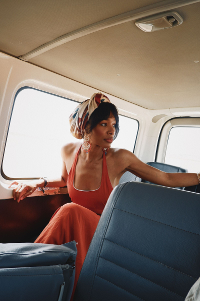 A photo of Claudya Moreira in an orange dress and headscarf sitting inside a car.
